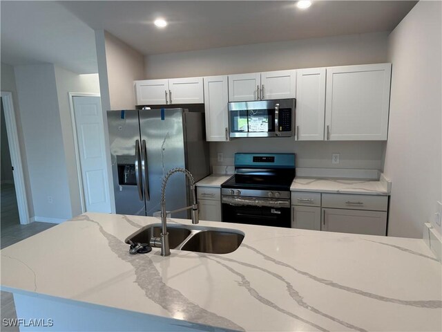 kitchen with light stone countertops, recessed lighting, white cabinetry, a sink, and appliances with stainless steel finishes