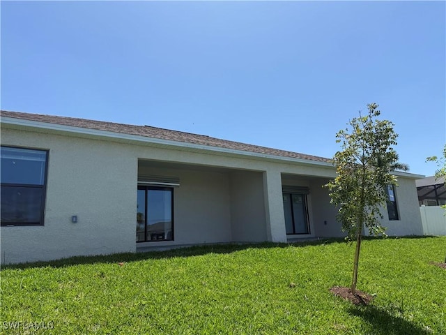 rear view of house featuring a lawn and stucco siding