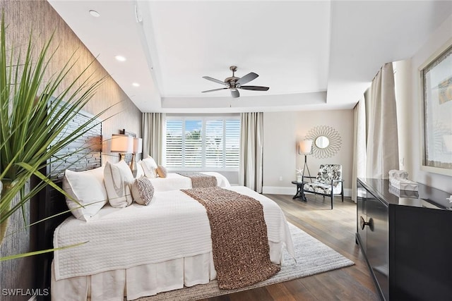 bedroom with a tray ceiling, wood finished floors, baseboards, and ceiling fan
