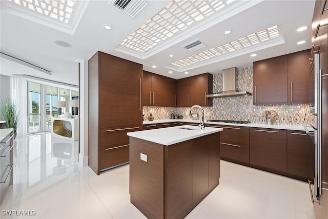 kitchen with backsplash, wall chimney range hood, modern cabinets, and a sink