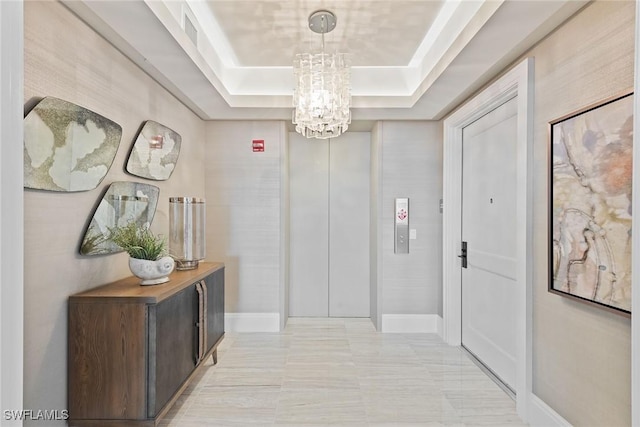 hall featuring an inviting chandelier, visible vents, baseboards, and a raised ceiling