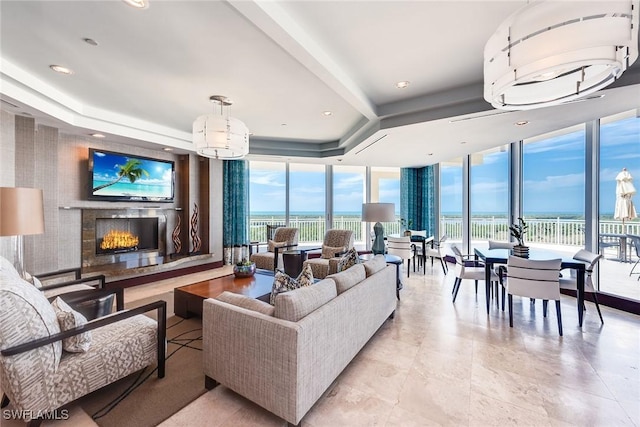 living area featuring a raised ceiling, a warm lit fireplace, recessed lighting, and floor to ceiling windows