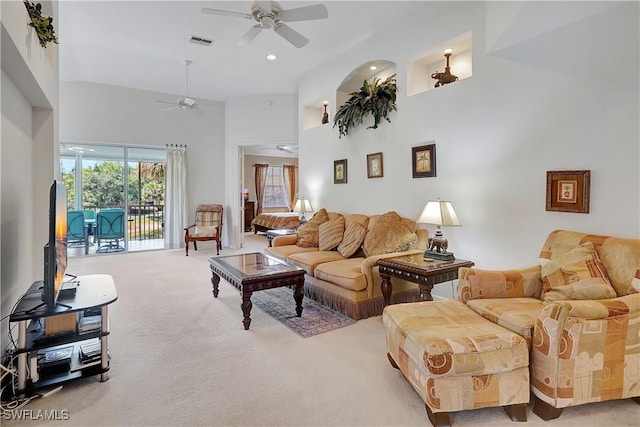 living area featuring ceiling fan, carpet flooring, a high ceiling, and visible vents