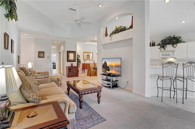 living room with a ceiling fan, recessed lighting, light colored carpet, and a towering ceiling