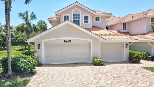 mediterranean / spanish house with stucco siding, a tile roof, decorative driveway, and a garage