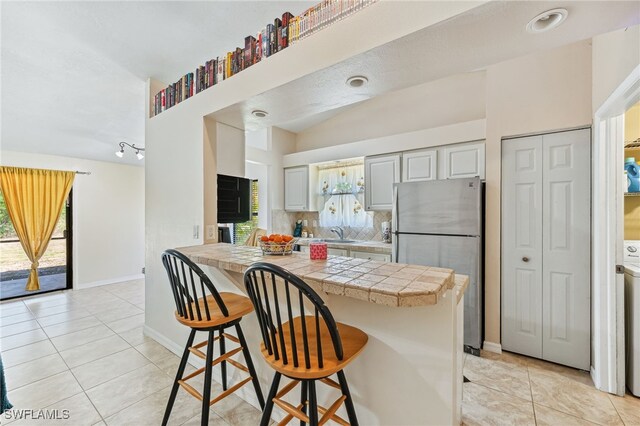 kitchen featuring a breakfast bar, freestanding refrigerator, a peninsula, decorative backsplash, and light tile patterned floors