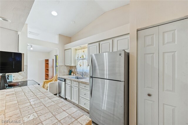 kitchen with decorative backsplash, appliances with stainless steel finishes, a sink, light countertops, and lofted ceiling
