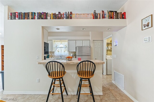 kitchen featuring a kitchen breakfast bar, freestanding refrigerator, a peninsula, washer / clothes dryer, and visible vents