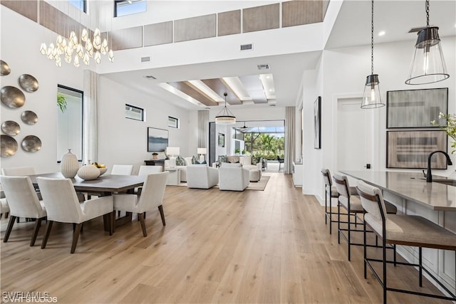 dining space featuring light wood-style floors, a towering ceiling, a chandelier, and visible vents