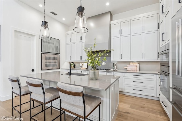 kitchen with visible vents, a kitchen breakfast bar, white cabinetry, a sink, and light wood-style flooring