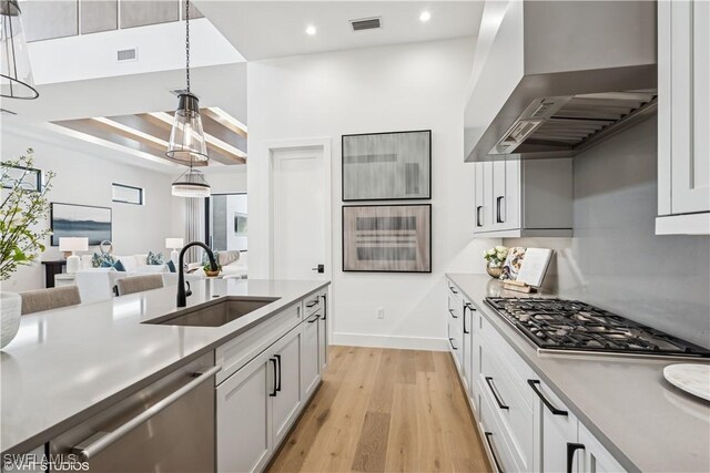 kitchen with wall chimney range hood, appliances with stainless steel finishes, a sink, light wood-type flooring, and visible vents