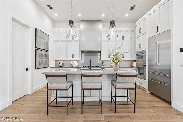 kitchen with white cabinets, stainless steel appliances, wall chimney exhaust hood, and visible vents