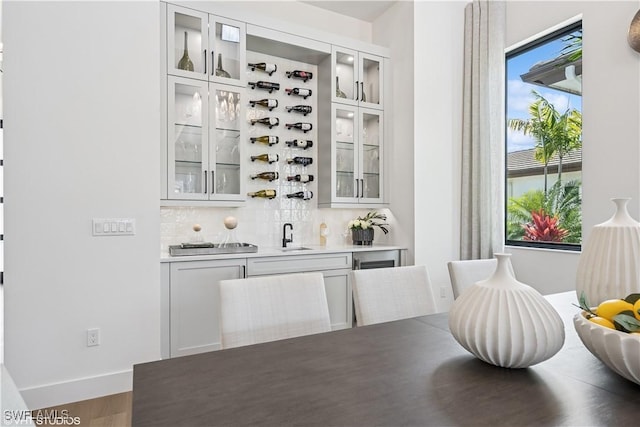 bar with wood finished floors, indoor wet bar, baseboards, a sink, and backsplash
