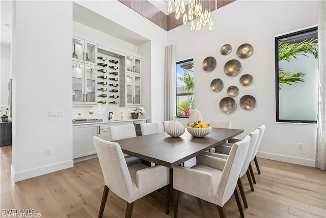 dining room featuring baseboards, light wood-style flooring, bar area, and a notable chandelier