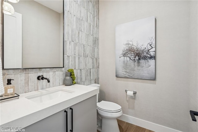 bathroom featuring vanity, toilet, baseboards, wood finished floors, and backsplash