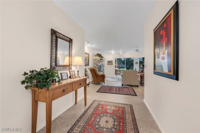 hall featuring light tile patterned floors, baseboards, and rail lighting