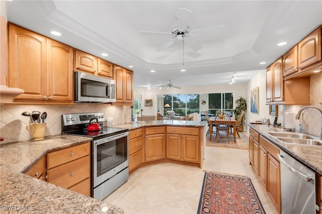 kitchen with ceiling fan, appliances with stainless steel finishes, a sink, recessed lighting, and a tray ceiling