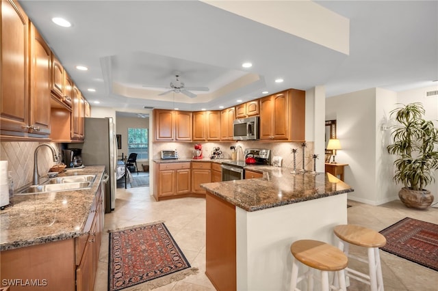 kitchen featuring a breakfast bar area, tasteful backsplash, a sink, dark stone countertops, and stainless steel appliances