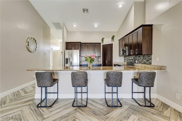 1045 SW Embers Ter, Cape Coral, FL 33991 - kitchen featuring stainless steel appliances, dark brown cabinets, light stone countertops, and backsplash