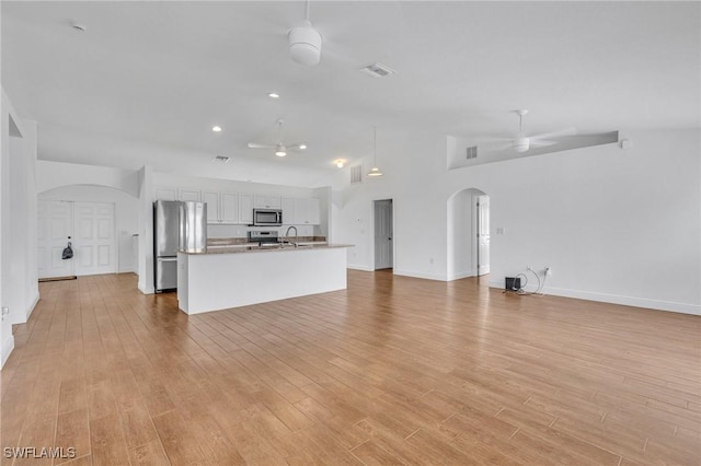 unfurnished living room with arched walkways, a ceiling fan, a sink, light wood-style floors, and vaulted ceiling