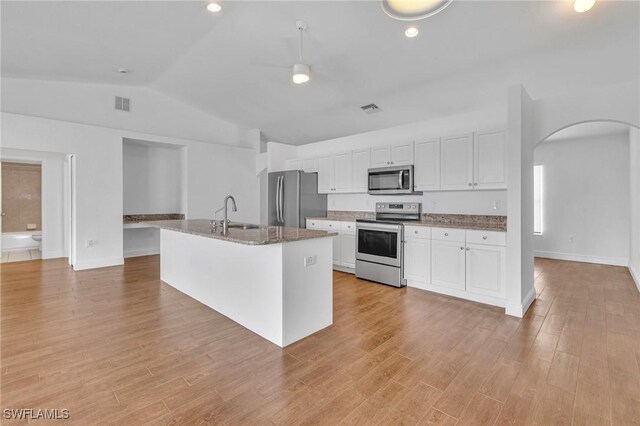 kitchen with appliances with stainless steel finishes, lofted ceiling, white cabinetry, arched walkways, and light wood-style flooring