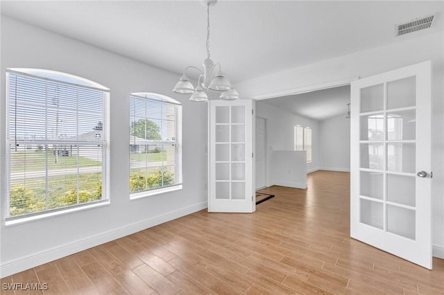 unfurnished dining area featuring baseboards, a chandelier, light wood-style floors, and french doors