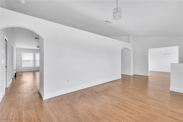 spare room featuring arched walkways, a chandelier, and light wood-style flooring