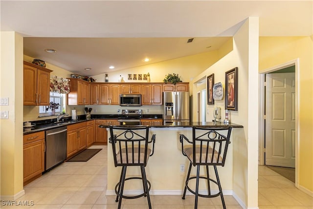 kitchen featuring dark countertops, a breakfast bar, stainless steel appliances, a peninsula, and vaulted ceiling