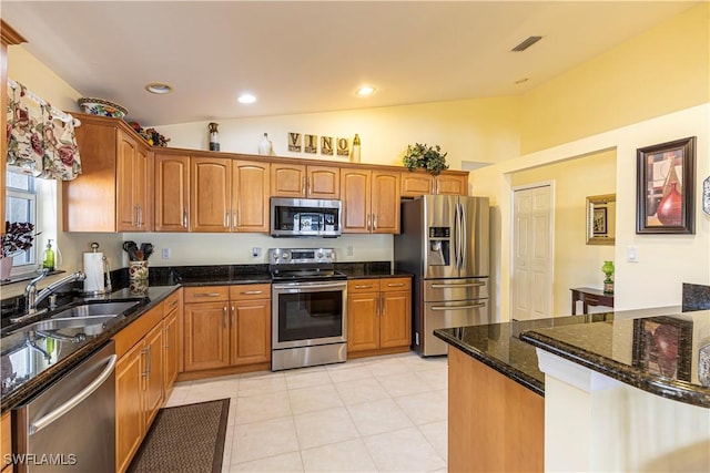 kitchen with appliances with stainless steel finishes, a sink, brown cabinetry, dark stone countertops, and visible vents