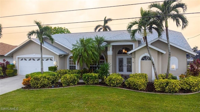 view of front facade with a garage, stucco siding, a front yard, french doors, and driveway