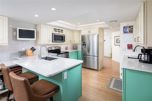 kitchen featuring a sink, stainless steel appliances, a peninsula, backsplash, and a tray ceiling