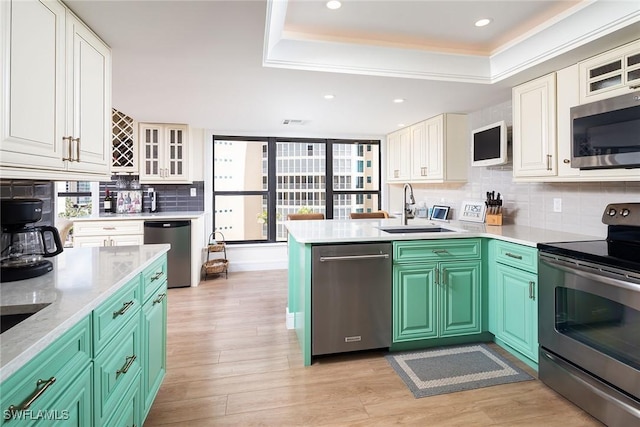 kitchen featuring white cabinets, a tray ceiling, tasteful backsplash, a sink, and appliances with stainless steel finishes