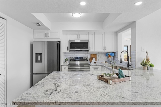 kitchen with backsplash, appliances with stainless steel finishes, a sink, light stone counters, and a peninsula