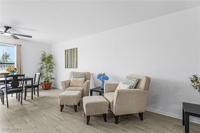living area featuring baseboards, a ceiling fan, and wood finish floors