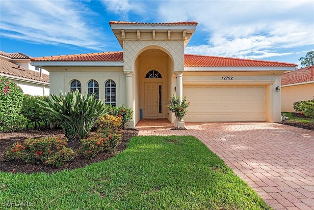 mediterranean / spanish-style house with stucco siding, a garage, a tiled roof, and decorative driveway