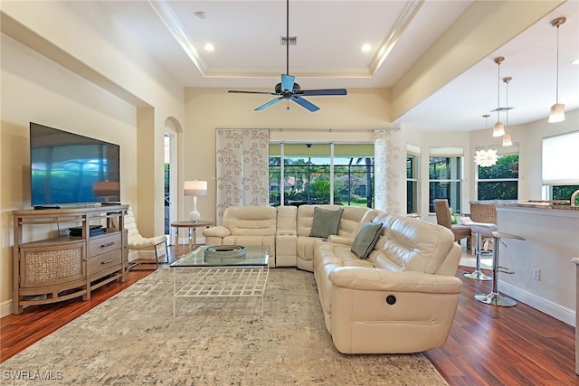 living room with a ceiling fan, a tray ceiling, crown molding, and wood finished floors