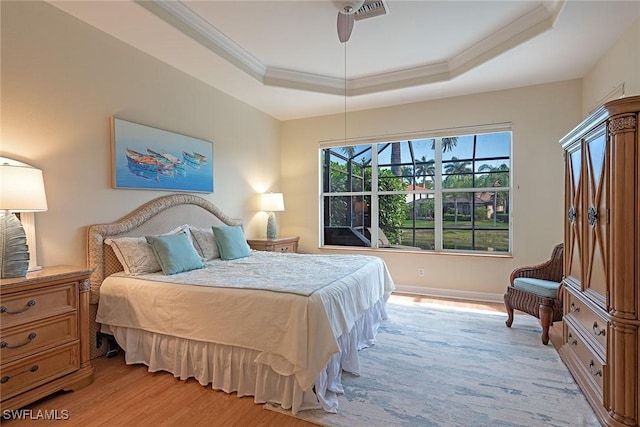 bedroom with a raised ceiling, ornamental molding, and light wood-style flooring