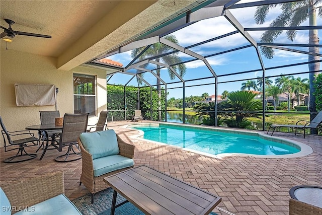 pool with a water view, glass enclosure, a patio, and ceiling fan