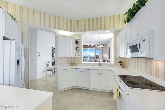 kitchen featuring a sink, white appliances, a chandelier, wallpapered walls, and light tile patterned floors