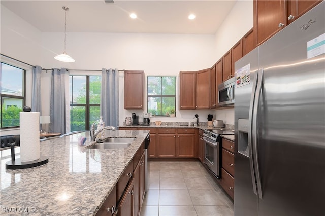 kitchen featuring pendant lighting, light stone countertops, a sink, appliances with stainless steel finishes, and light tile patterned floors