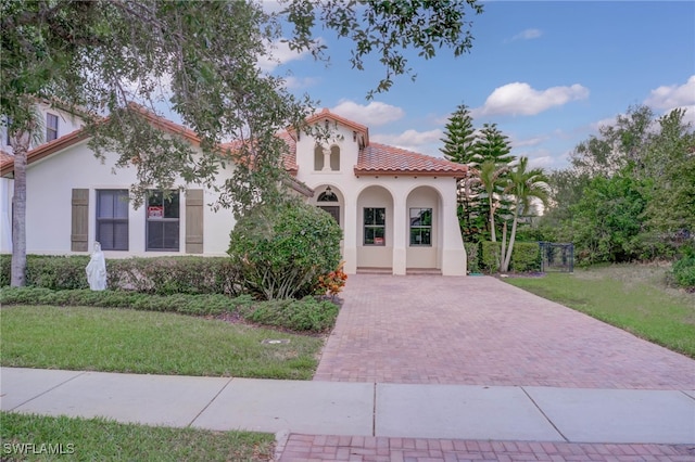 mediterranean / spanish-style house featuring stucco siding, a tile roof, and a front yard