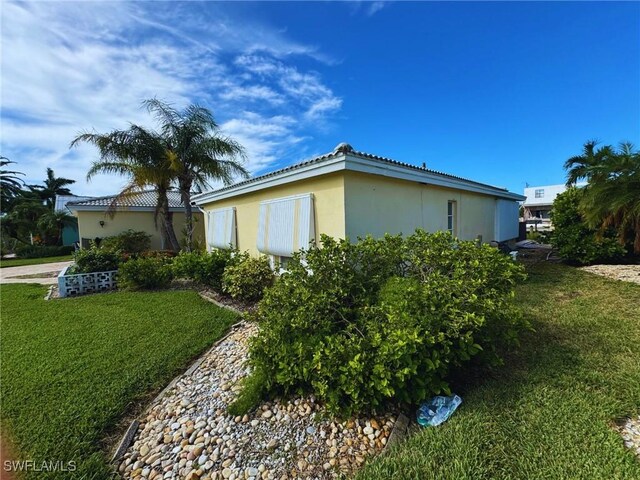 12 Bayview Blvd, Fort Myers Beach, FL 33931 - view of side of property with a lawn, a tiled roof, and stucco siding