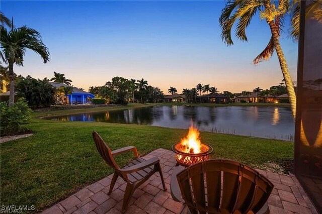 4009 Treadwater Ct, Naples, FL 34109 - patio terrace at dusk featuring a water view, a yard, and an outdoor fire pit