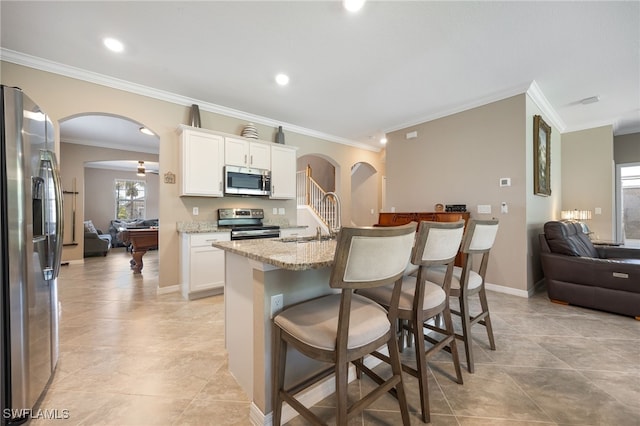 kitchen with a breakfast bar area, a sink, open floor plan, arched walkways, and appliances with stainless steel finishes