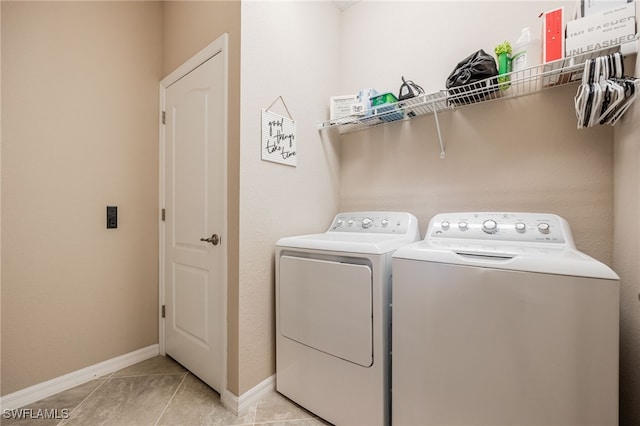 clothes washing area with light tile patterned floors, baseboards, washing machine and dryer, and laundry area