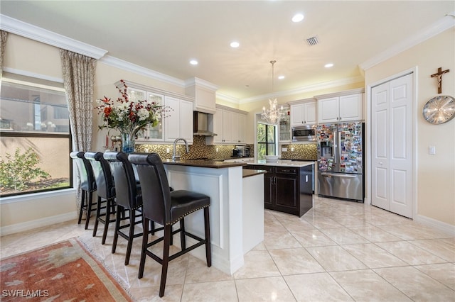 3412 Atlantic Cir, Naples, FL 34119 - kitchen featuring wall chimney range hood, backsplash, visible vents, appliances with stainless steel finishes, and an inviting chandelier