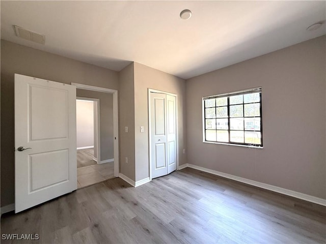 unfurnished bedroom with baseboards, a closet, wood finished floors, and visible vents