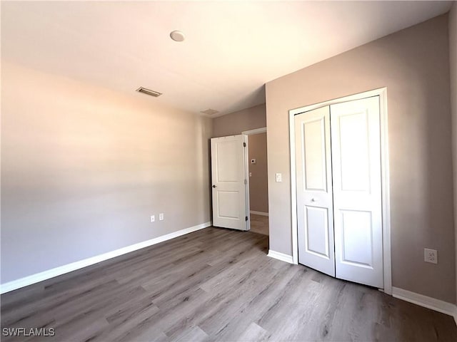 unfurnished bedroom with baseboards, a closet, wood finished floors, and visible vents