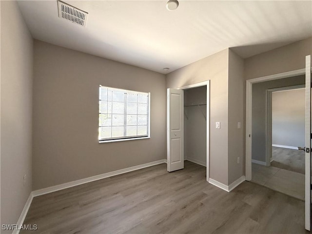 unfurnished bedroom with baseboards, a closet, wood finished floors, and visible vents
