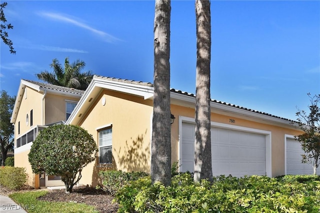 view of side of home with an attached garage, stucco siding, and a tiled roof